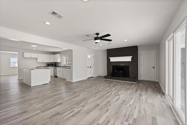 unfurnished living room featuring a brick fireplace, ceiling fan, and light hardwood / wood-style flooring