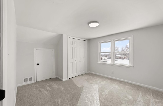 unfurnished bedroom with lofted ceiling, light colored carpet, and a closet