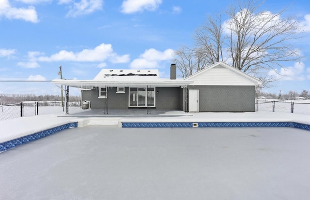 snow covered house featuring an empty pool and a patio