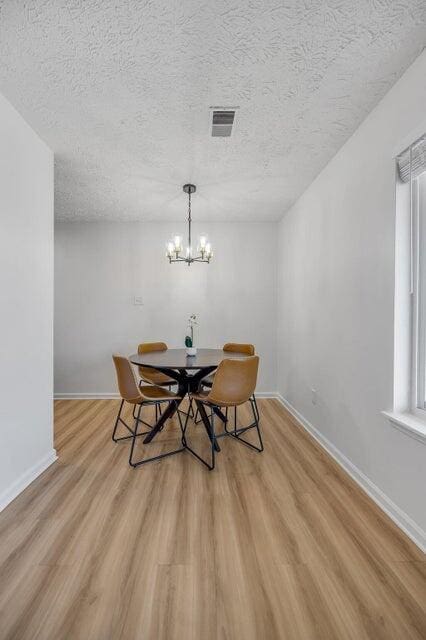 unfurnished dining area with a textured ceiling, light hardwood / wood-style floors, and a notable chandelier