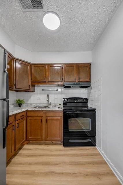 kitchen featuring decorative backsplash, light wood-type flooring, sink, black range with electric stovetop, and stainless steel refrigerator