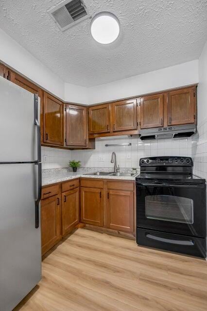 kitchen with backsplash, sink, light hardwood / wood-style flooring, stainless steel fridge, and black range with electric cooktop