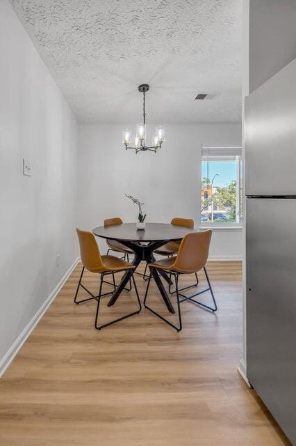 dining area with a textured ceiling, light hardwood / wood-style flooring, and an inviting chandelier