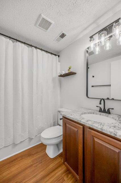 full bathroom featuring shower / bathtub combination with curtain, wood-type flooring, a textured ceiling, toilet, and vanity