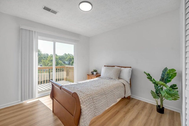 bedroom with a textured ceiling, access to outside, and light hardwood / wood-style flooring