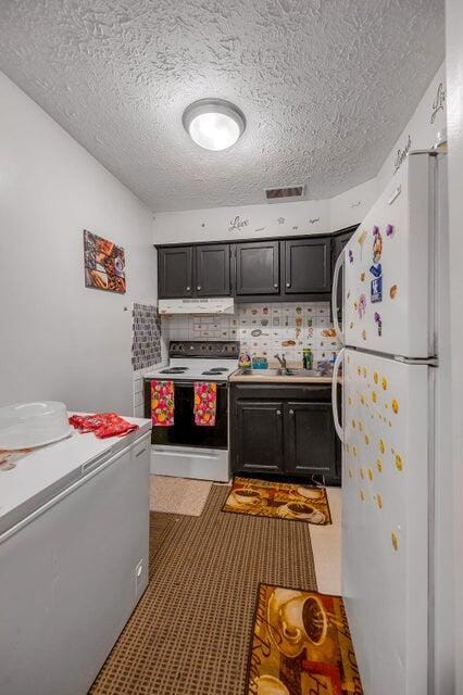 kitchen with electric range oven, tasteful backsplash, a textured ceiling, sink, and white fridge