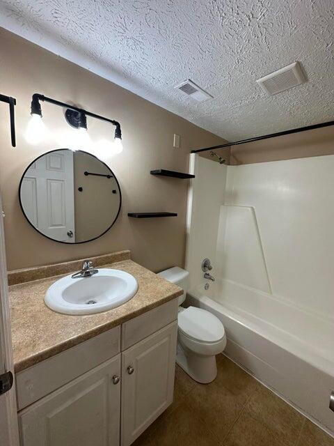 full bathroom featuring vanity, toilet, a textured ceiling, and bathtub / shower combination