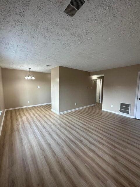 unfurnished living room featuring hardwood / wood-style flooring, a textured ceiling, and a chandelier