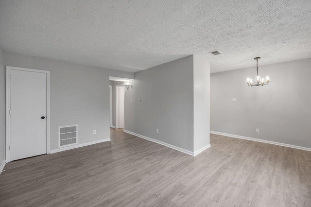 spare room with a textured ceiling, light hardwood / wood-style flooring, and an inviting chandelier