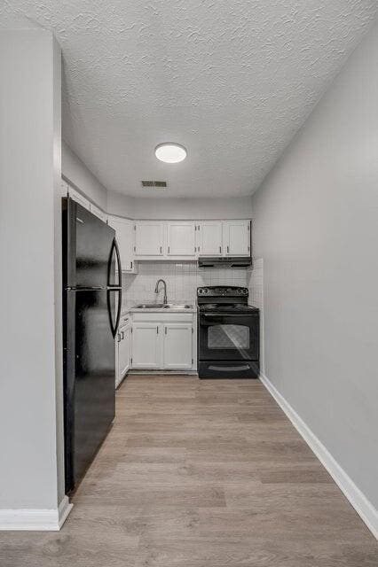 kitchen with backsplash, light hardwood / wood-style floors, a textured ceiling, white cabinets, and black appliances