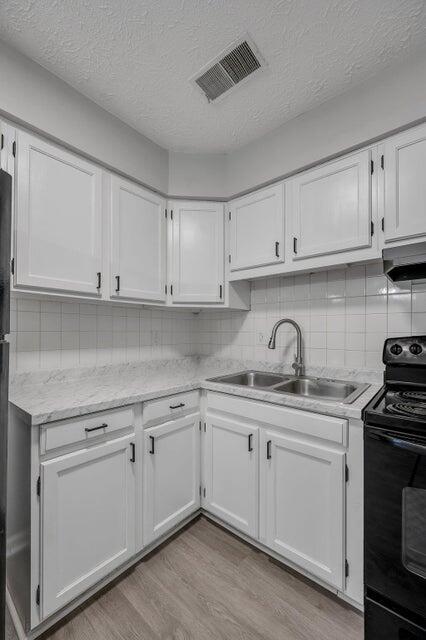 kitchen featuring black range with electric stovetop, sink, a textured ceiling, white cabinets, and light wood-type flooring