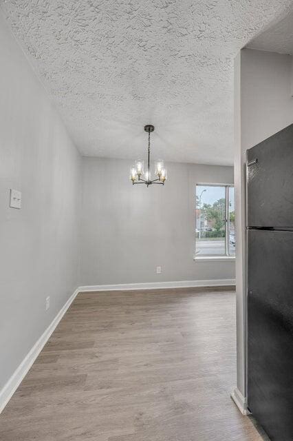 unfurnished dining area featuring a chandelier, wood-type flooring, and a textured ceiling