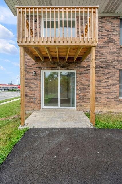 property entrance with a lawn, a balcony, and a patio