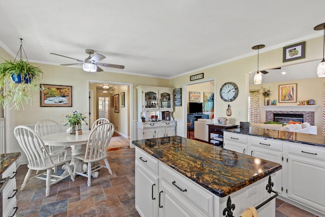 kitchen with white cabinetry, ceiling fan, dark stone countertops, decorative light fixtures, and a fireplace