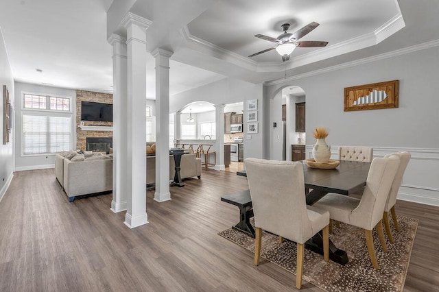 dining area with ceiling fan, crown molding, hardwood / wood-style floors, a tray ceiling, and a fireplace