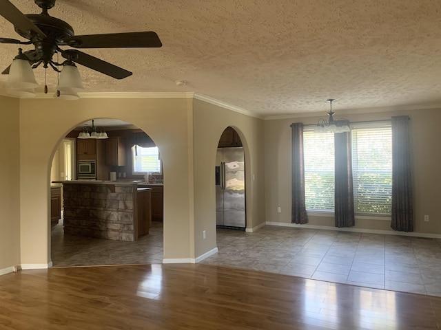 spare room featuring a textured ceiling, ceiling fan with notable chandelier, light hardwood / wood-style floors, and crown molding