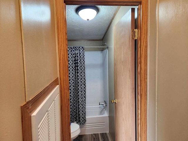 bathroom featuring hardwood / wood-style flooring, toilet, shower / bathtub combination with curtain, and a textured ceiling