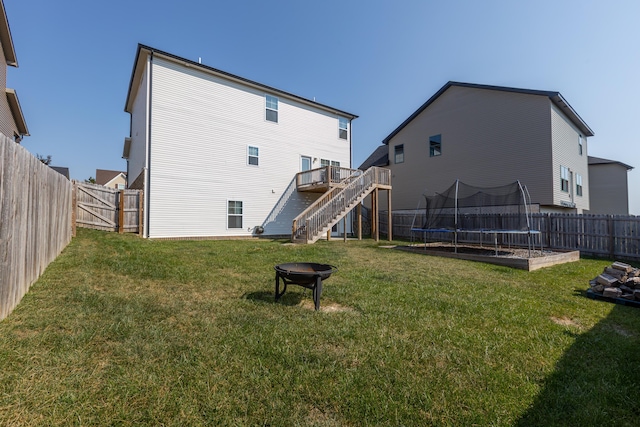 rear view of property with a lawn, a fire pit, and a trampoline