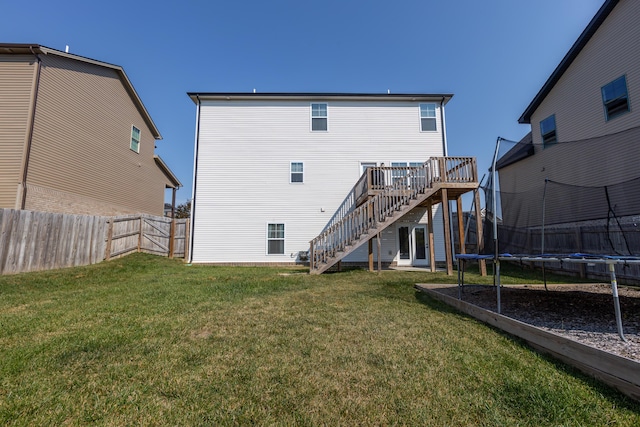 back of house featuring a lawn, a wooden deck, and a trampoline