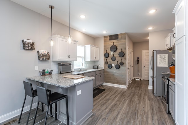 kitchen featuring pendant lighting, kitchen peninsula, stainless steel electric range oven, a kitchen bar, and white cabinetry