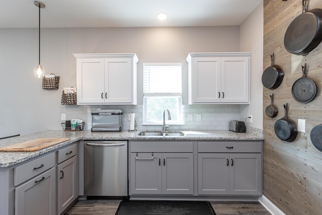 kitchen featuring wooden walls, sink, decorative light fixtures, dishwasher, and white cabinetry