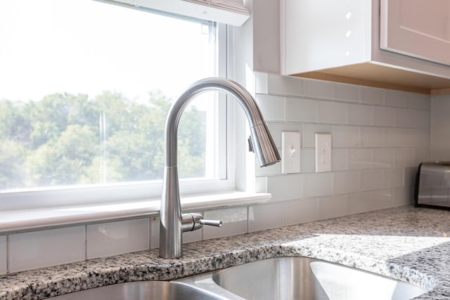 details featuring white cabinetry, decorative backsplash, sink, and light stone countertops