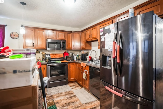 kitchen with a textured ceiling, light hardwood / wood-style flooring, decorative light fixtures, stainless steel appliances, and sink