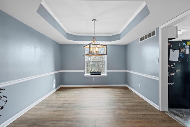 unfurnished dining area with a raised ceiling, wood-type flooring, and ornamental molding