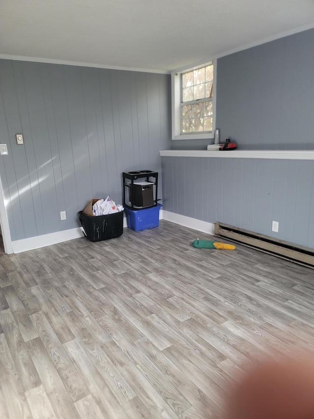 interior space with baseboard heating, wood walls, light hardwood / wood-style floors, and ornamental molding