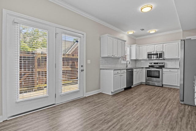 kitchen with backsplash, appliances with stainless steel finishes, crown molding, white cabinets, and light wood-type flooring