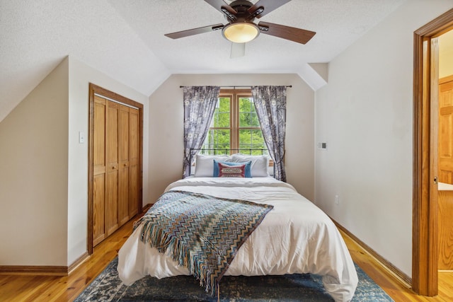 bedroom featuring ceiling fan, vaulted ceiling, light hardwood / wood-style flooring, a textured ceiling, and a closet