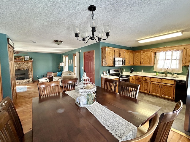 dining space featuring a fireplace, sink, light hardwood / wood-style flooring, a textured ceiling, and a chandelier