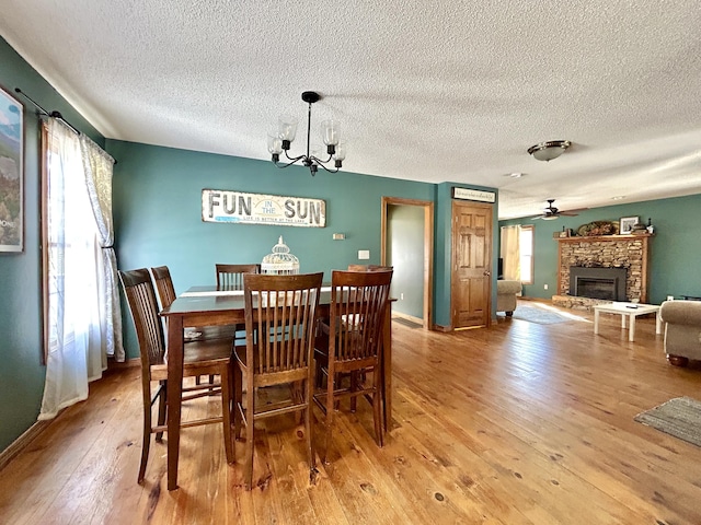 dining area featuring light hardwood / wood-style floors, ceiling fan with notable chandelier, and a fireplace