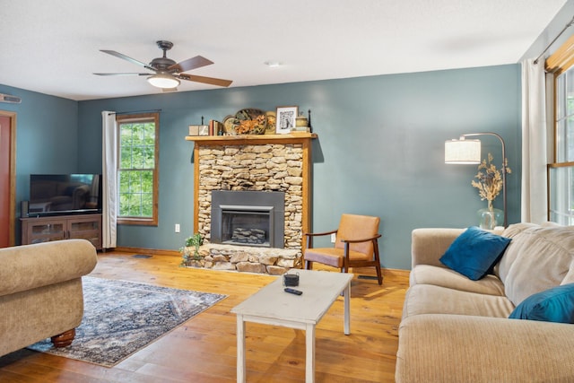 living room featuring hardwood / wood-style flooring, ceiling fan, and a stone fireplace