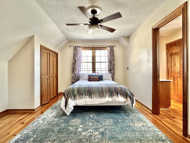 bedroom with ceiling fan, a textured ceiling, hardwood / wood-style flooring, and vaulted ceiling