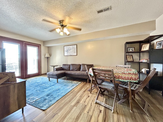 living room with ceiling fan, a textured ceiling, french doors, and light wood-type flooring