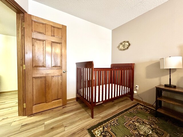 bedroom with light wood-type flooring, a nursery area, and a textured ceiling