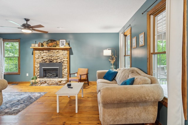 living room with ceiling fan, wood-type flooring, and a stone fireplace