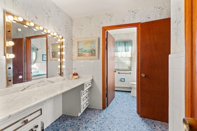 bathroom with toilet, vanity, tile patterned floors, tile walls, and a baseboard radiator