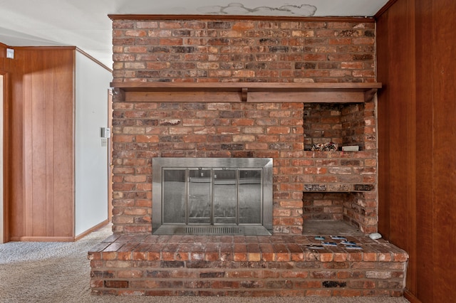 details with a brick fireplace, wooden walls, carpet flooring, and ornamental molding