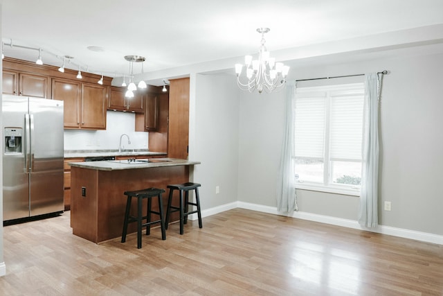 kitchen featuring stainless steel refrigerator with ice dispenser, decorative light fixtures, light hardwood / wood-style floors, and kitchen peninsula