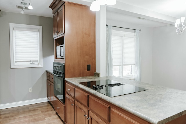 kitchen featuring pendant lighting, kitchen peninsula, light hardwood / wood-style flooring, and black appliances