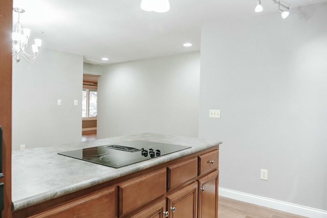 kitchen with black electric cooktop, an inviting chandelier, hanging light fixtures, and light wood-type flooring