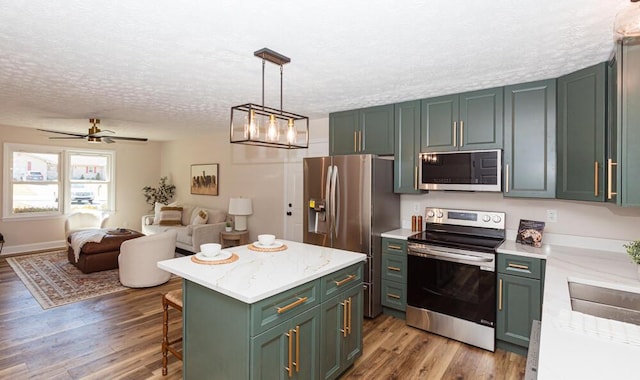 kitchen featuring a textured ceiling, stainless steel appliances, a kitchen island, wood finished floors, and green cabinetry