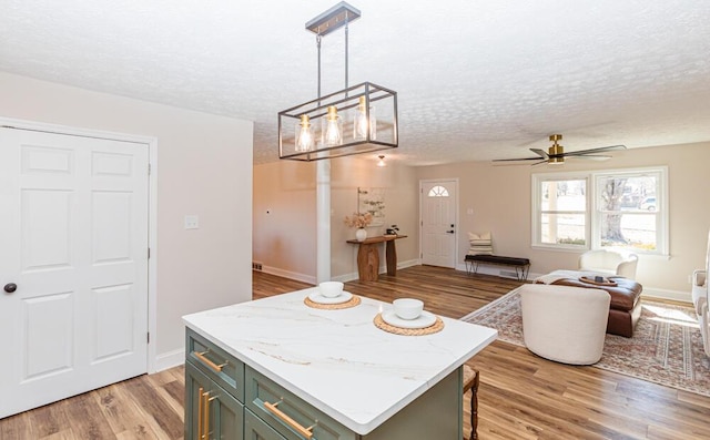 kitchen featuring ceiling fan, open floor plan, hanging light fixtures, a textured ceiling, and light wood-type flooring