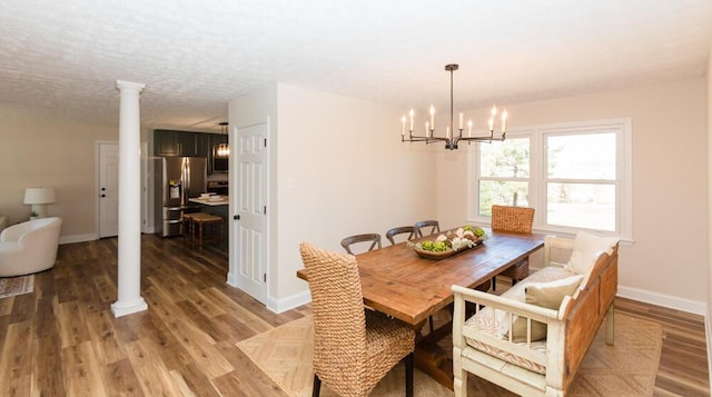 dining room featuring a textured ceiling, a notable chandelier, baseboards, light wood finished floors, and decorative columns