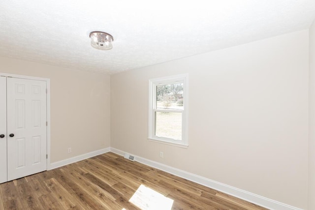 spare room with visible vents, a textured ceiling, baseboards, and wood finished floors