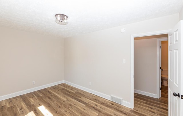 empty room featuring a textured ceiling, wood finished floors, visible vents, and baseboards