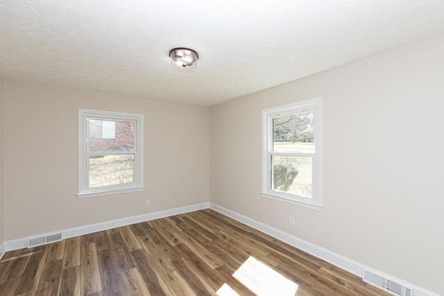 unfurnished room featuring baseboards, visible vents, and wood finished floors