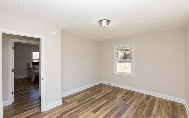 empty room featuring a textured ceiling, baseboards, and wood finished floors